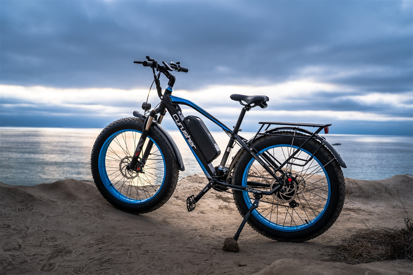 A Cyrusher XF650 electric bicycle is parked on the sand